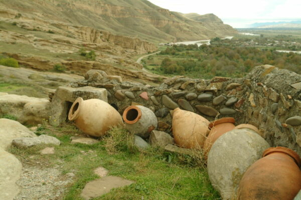 earthen jars set alongside a stone wall surrouded by mountains